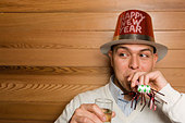 Man wearing Happy New Year party hat and blowing noise maker - Image AXMHX5 © JUPITERIMAGES/ Creatas 