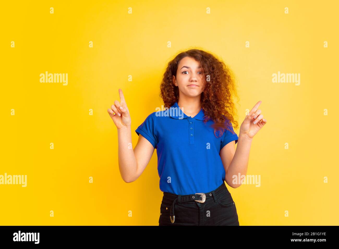 Pointing up, cute. Caucasian teen's girl portrait on yellow studio ...