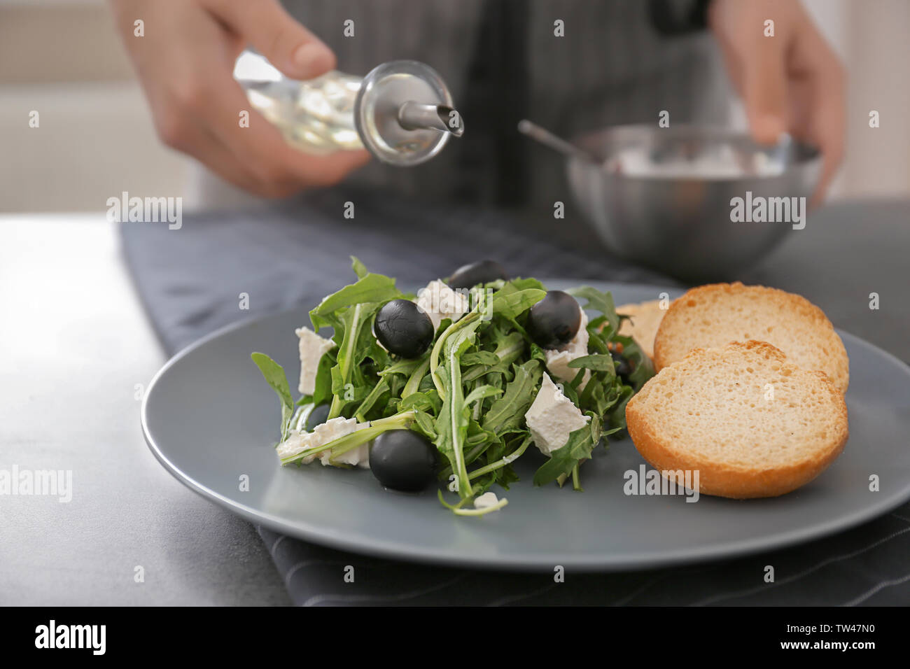 Woman dressing fresh vegetable salad with arugula leaves and olives ...