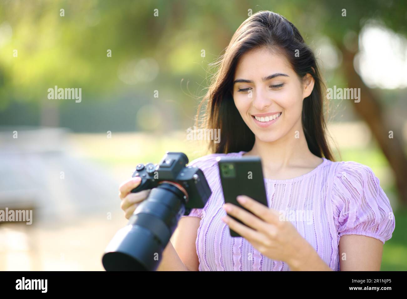 Happy photographer using phone and mirrorless camera in a park Stock ...