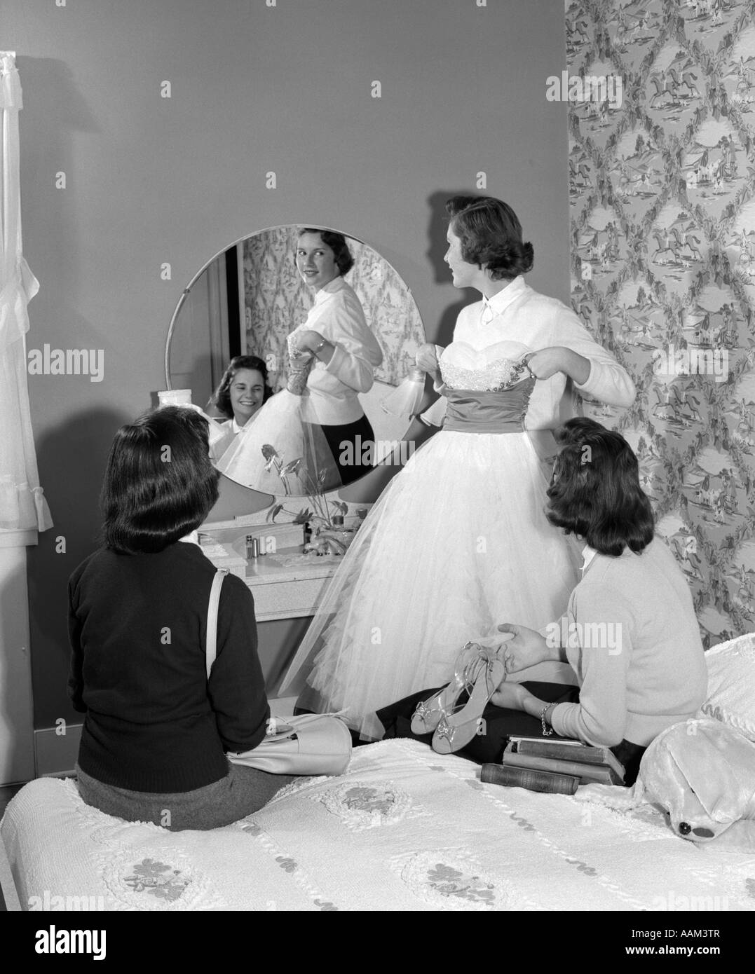 1950s TEEN GIRL HOLDING UP PROM DRESS TO MIRROR AS TWO GIRLFRIENDS ...
