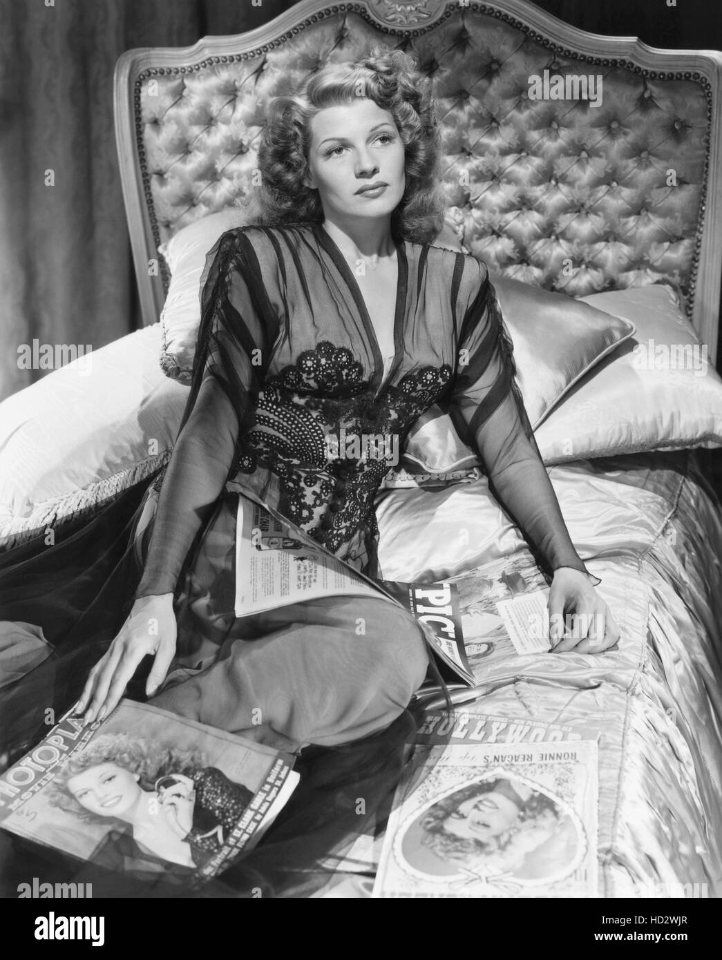 Rita Hayworth sitting on a bed with movie magazines featuring her image ...