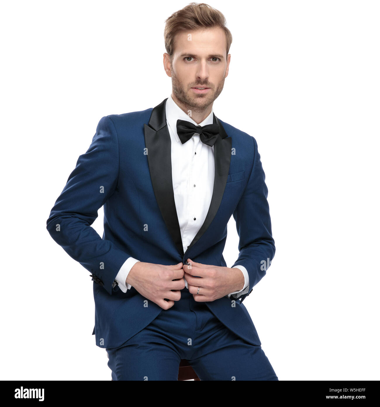 luxury man in blue tuxedo buttoning his lounge jacket while sitting on ...