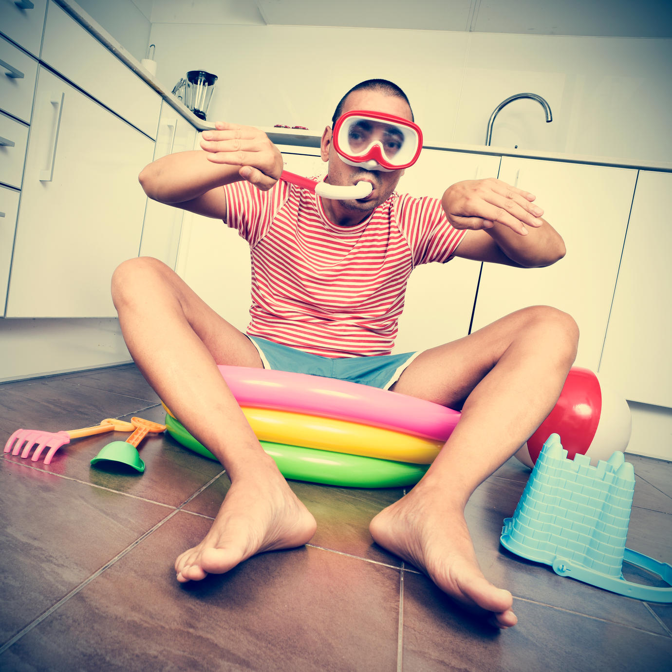 young man wearing a diving mask and a snorkel pretending he is swimming into an inflatable water pool, placed in the kitchen, wi