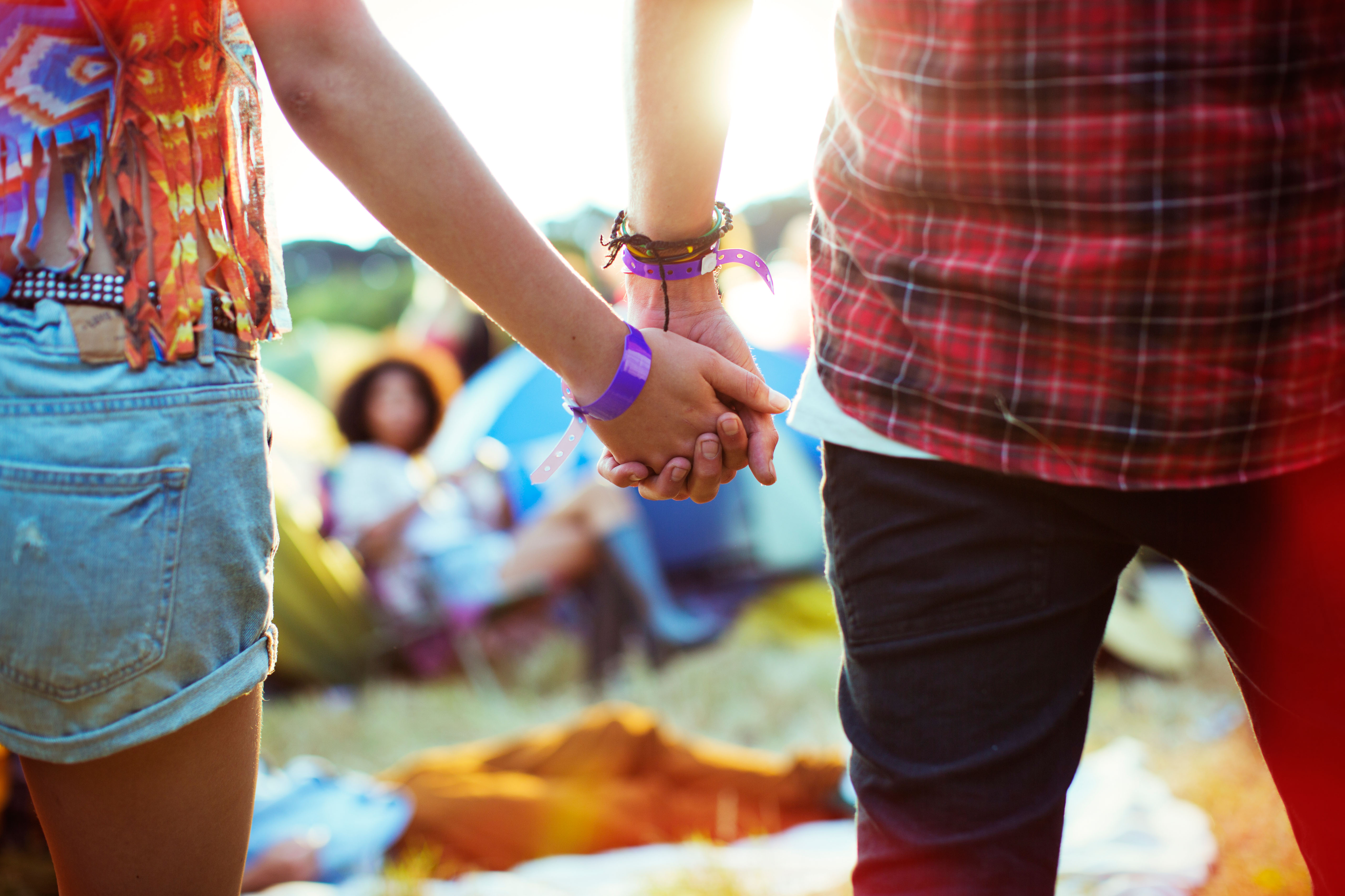 Close up of couple holding hands outside tents at music festival. Image shot 2012. Exact date unknown.
